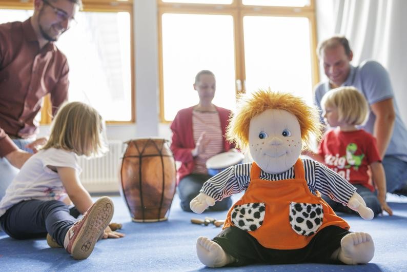 Zwei spielende Kinder mit ihren Vätern und der Lehrkraft im Musikgarten