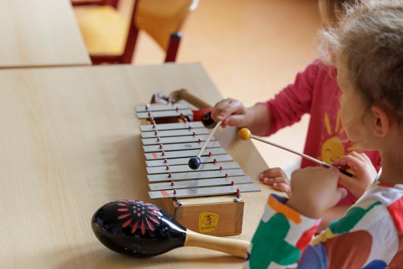 Zwei spielende Kinder mit ihren Vätern und der Lehrkraft im Musikgarten