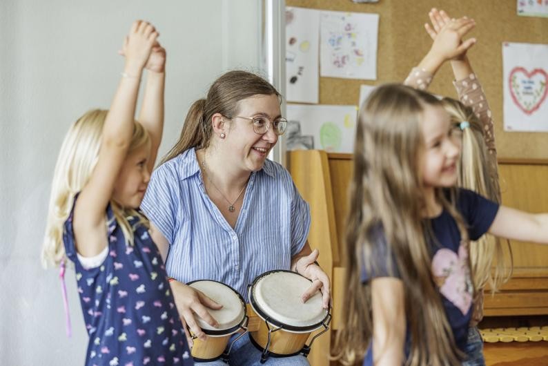 Drei spielende Mädchen und eine Lehrerin mit Trommeln bei der musikalischen Früherziehung