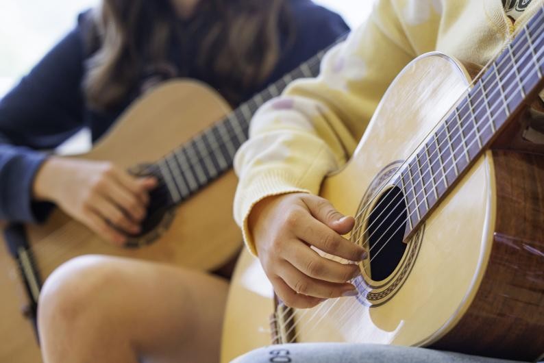 Zwei Mädchen spielen auf einer Akkustik-Gitarre